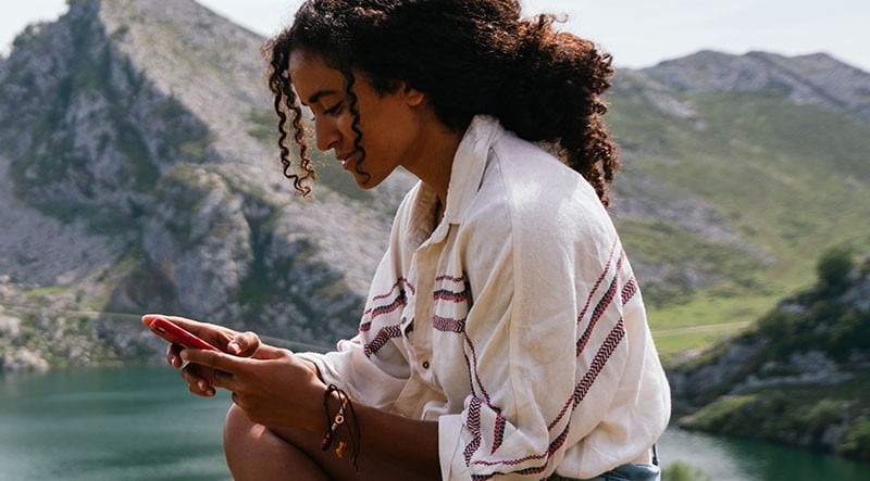 A woman looking at her phone with a mountain in the background.