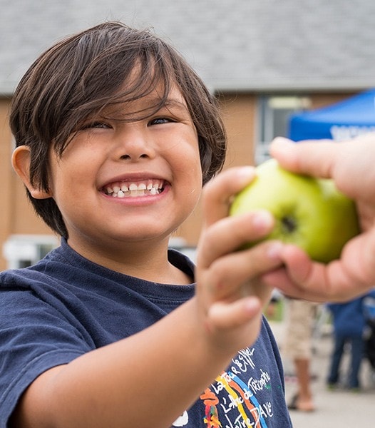 a happy kid taking an apple from a volunteer