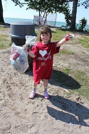 A little girl holding a bag of recycles and trash giving a thumbs up