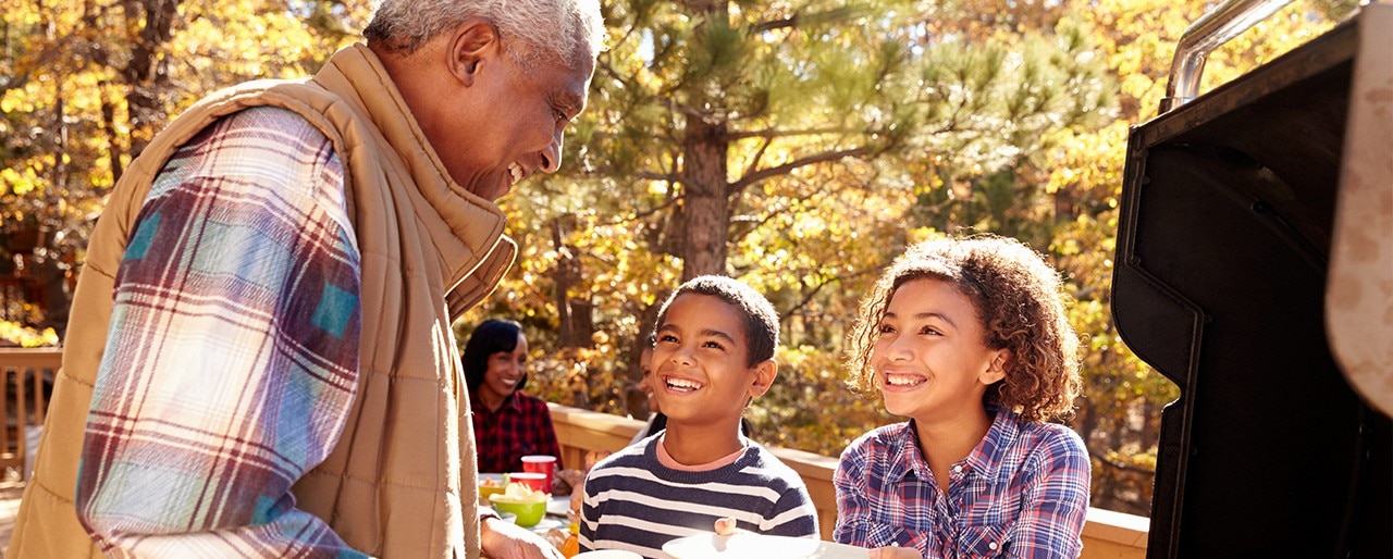 A man barbecues as his two grandchildren wait for a burger.
