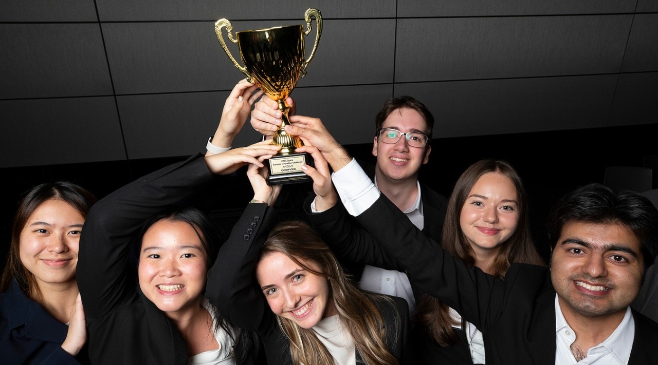 Six students stand together, collectively holding up a trophy in the air.