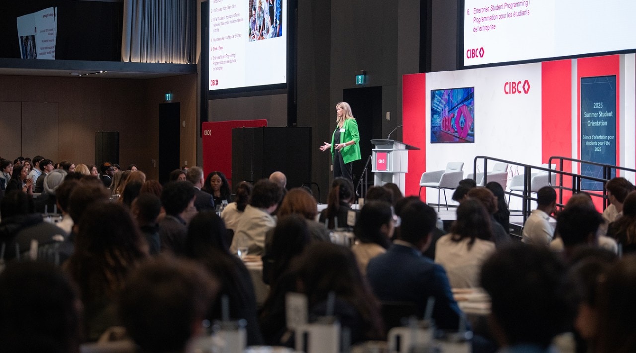 Student workshop participants sit at tables in a conference room watching a presentation by a CIBC leader.