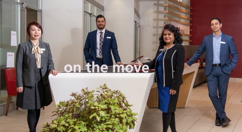 Four CIBC Banking Centre employees gathered around a desk. The words "on the move" sit atop the desk. 