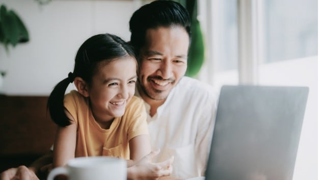 Un homme et sa fille regardent un ordinateur portatif ensemble et sourient.