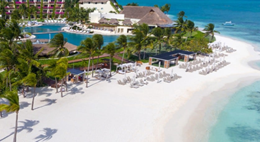 Plage tropicale avec des palmiers et des chaises de plage au premier plan et un centre de villégiature en arrière-plan.