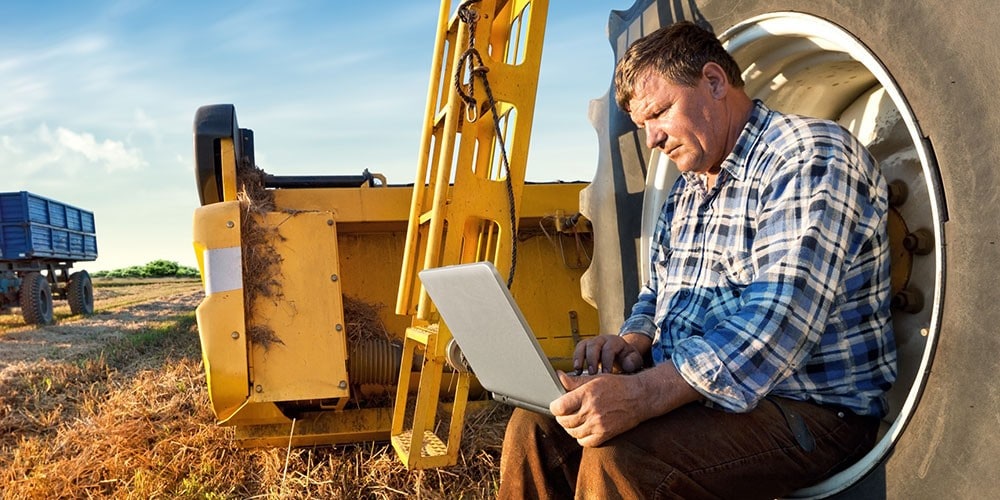 Farmer using a laptop while sitting outside.