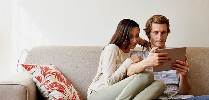 Un couple assis sur un canapé regarde une tablette.