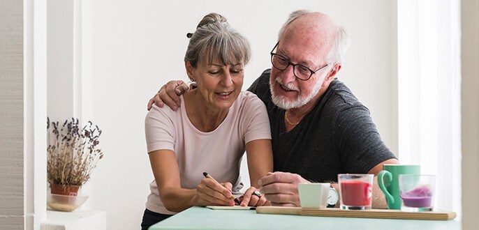 Un homme et une femme âgés sont assis ensemble à une table et discutent tout en prenant des notes.