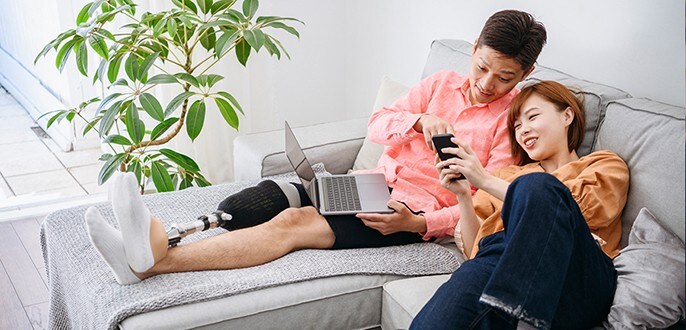 Un jeune couple relaxe sur un canapé tout en regardant un ordinateur portable et un téléphone