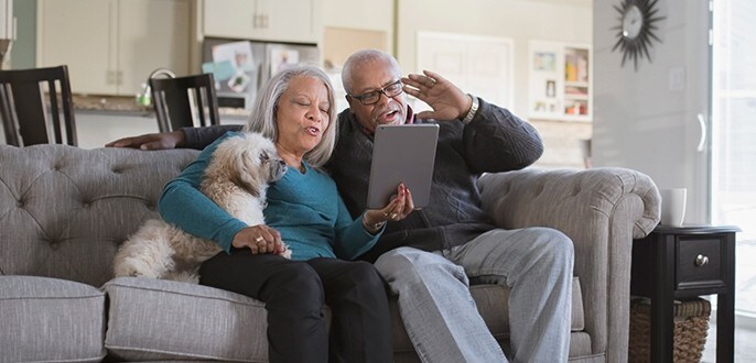 Un couple âgé est assis avec leur chien sur un canapé et regarde une tablette.
