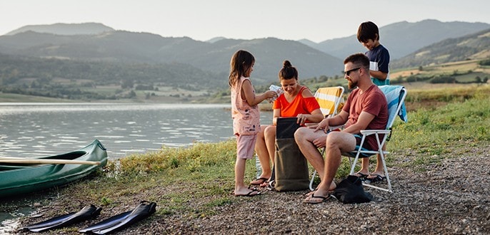 Un couple et leurs deux enfants se détendent au bord d’un lac où se trouve leur canoë.