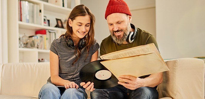 A father and his daughter seated on a couch checking out a vinyl record.