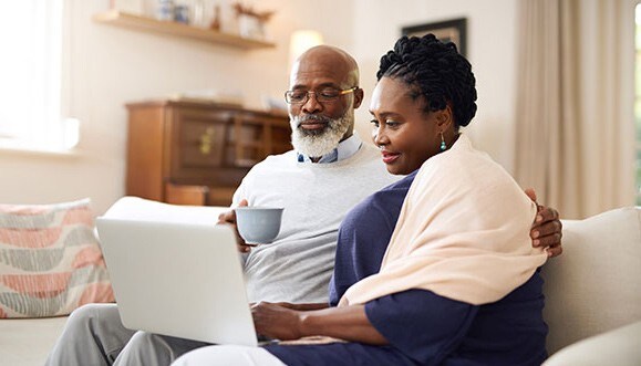 Un couple assis sur un canapé examine différentes options d’investissement sur un ordinateur portatif