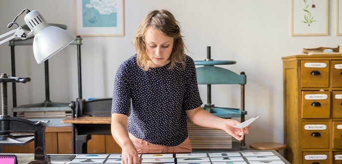 A woman laying down photos of ceramics on a desk in a studio.