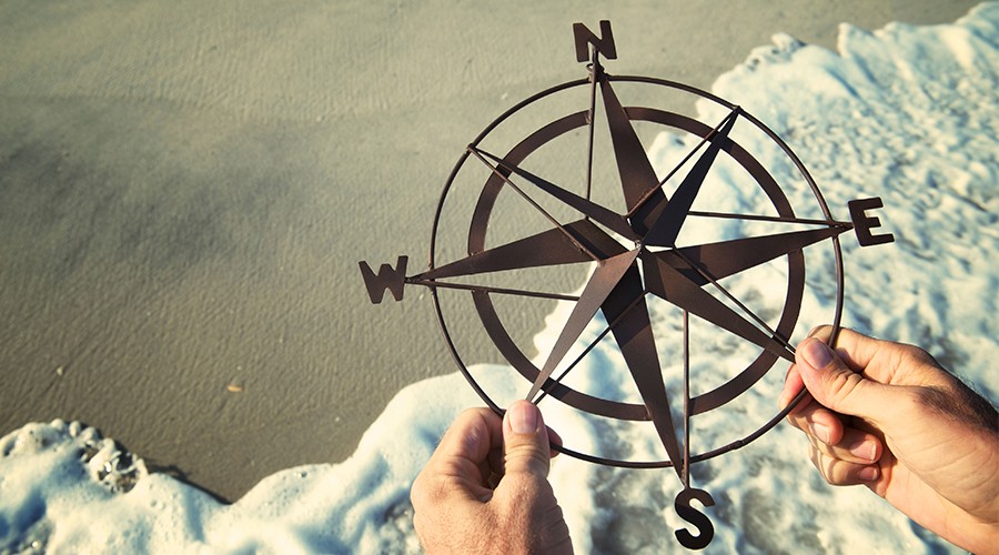 A man holding a metal compass rose on a beach