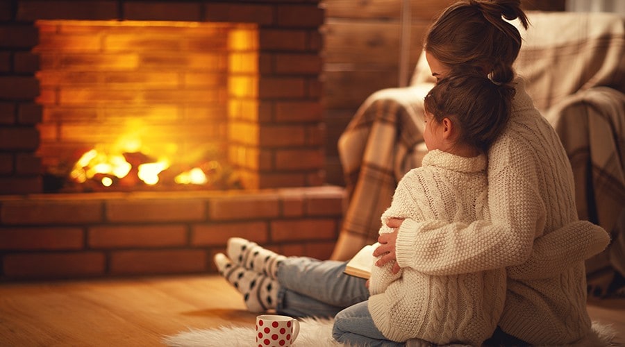 A mother and her daughter snuggled up by their fireplace