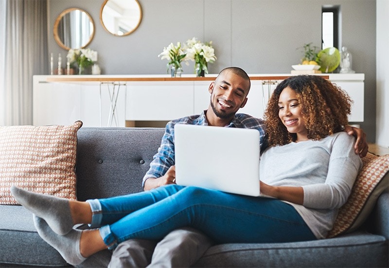 A happy couple using their laptop on their couch