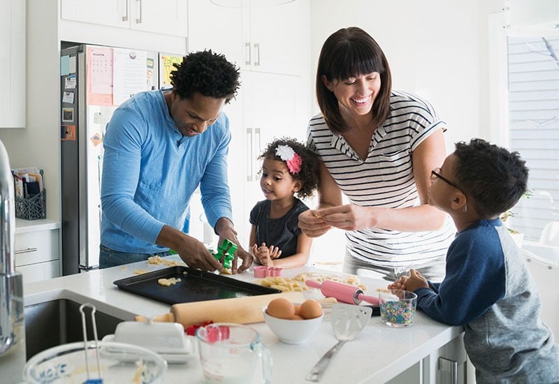 A married couple baking cookies with their toddlers