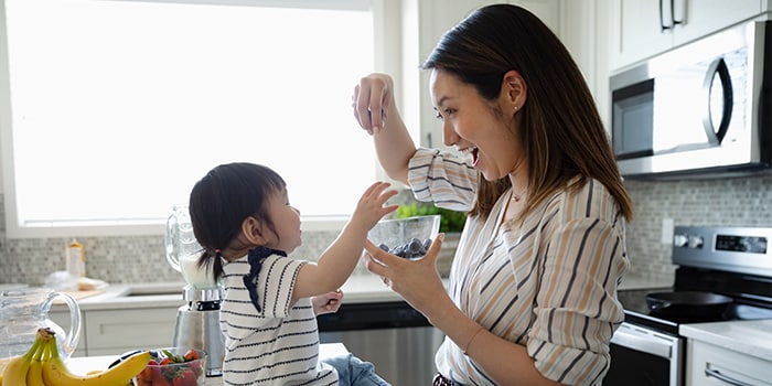 Une jeune femme qui s’amuse avec son enfant pendant qu’elle prépare un frappé aux fruits