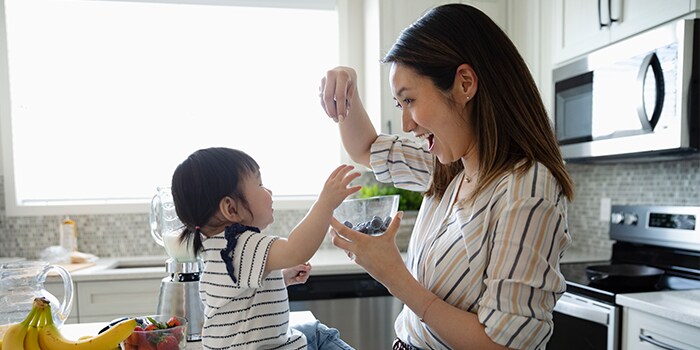 A young woman being playful with her kid while preparing a fruit smoothie
