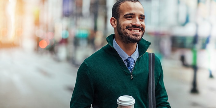 A well-dressed young man on the street, holding his coffee