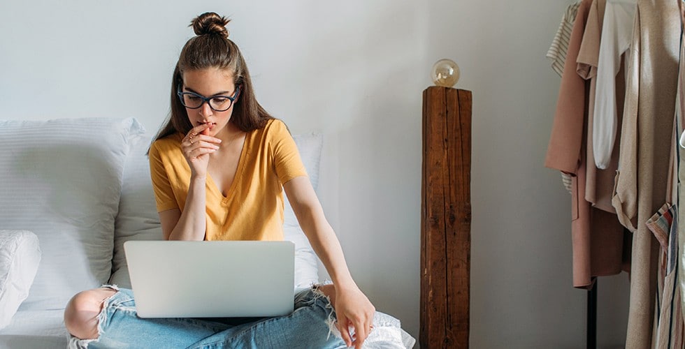 Une femme assise sur son lit regarde son ordinateur portatif