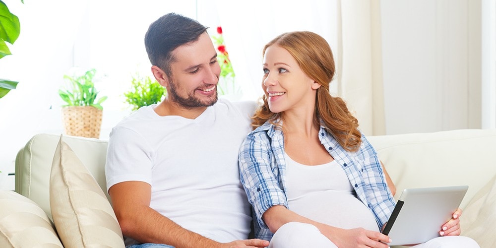 A husband and his pregnant wife smiling at each other