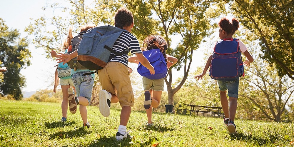 Children with backpacks running through the park