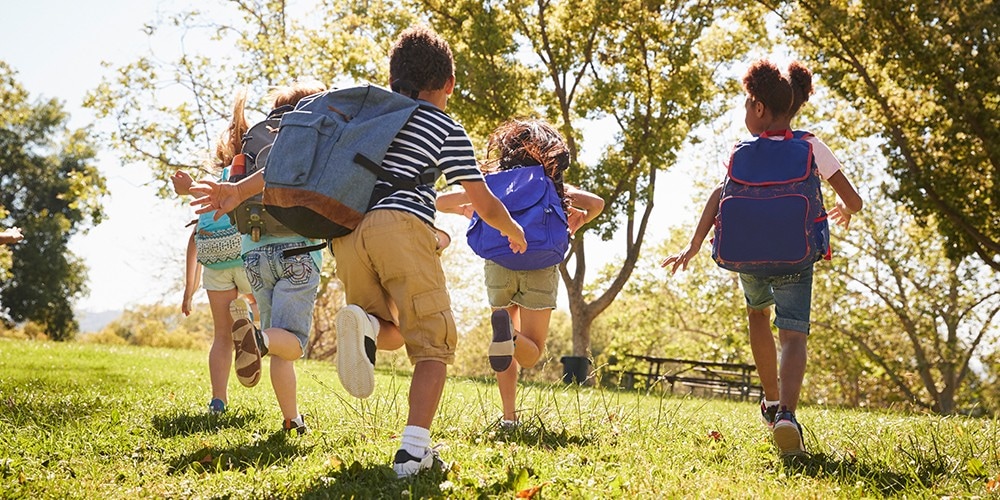 Children with backpacks running through the park