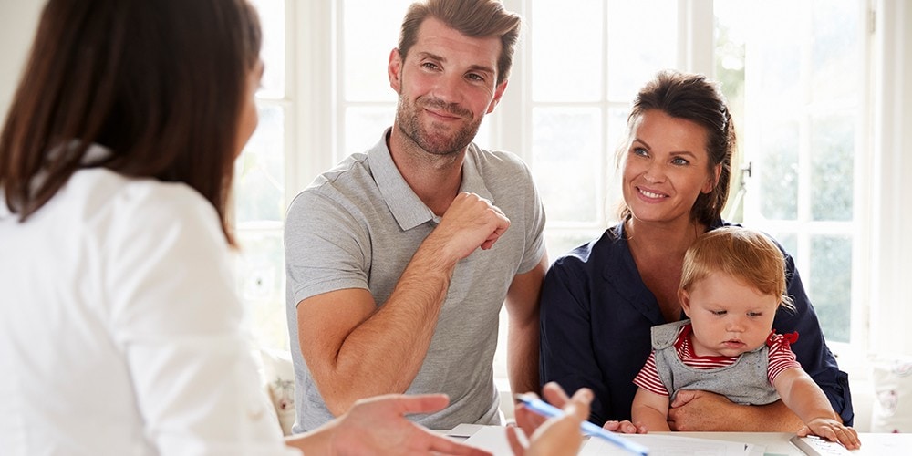 A mother holding her baby while she and her husband are talking with a financial advisor