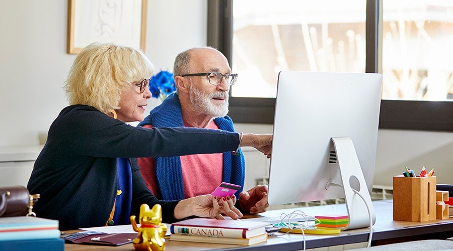 A senior couple shops online on their computer.