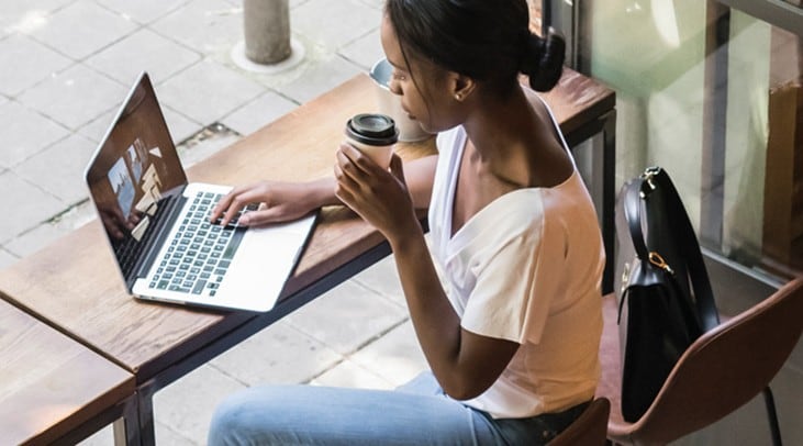 Woman registering for Autodeposit on her laptop while drinking a coffee