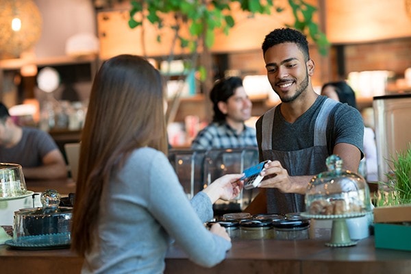 A woman tapping her credit card on a point of sale terminal in a coffeeshop