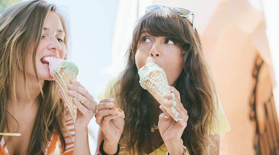 Two teen girls eat ice cream cones.
