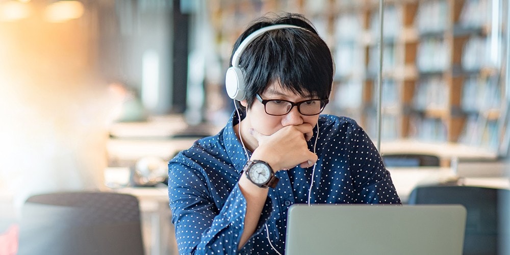 Student with headphones using a laptop in a library