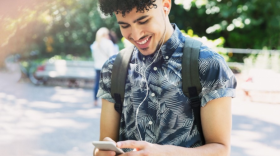 Un étudiant avec des écouteurs et un sac à dos utilise son téléphone intelligent