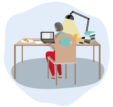 Une femme est assise à son bureau, où il y a un ordinateur portatif, une lampe, des livres et de la nourriture