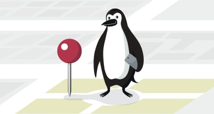 Percy Penguin standing next to a location marker with a phone in his hand.