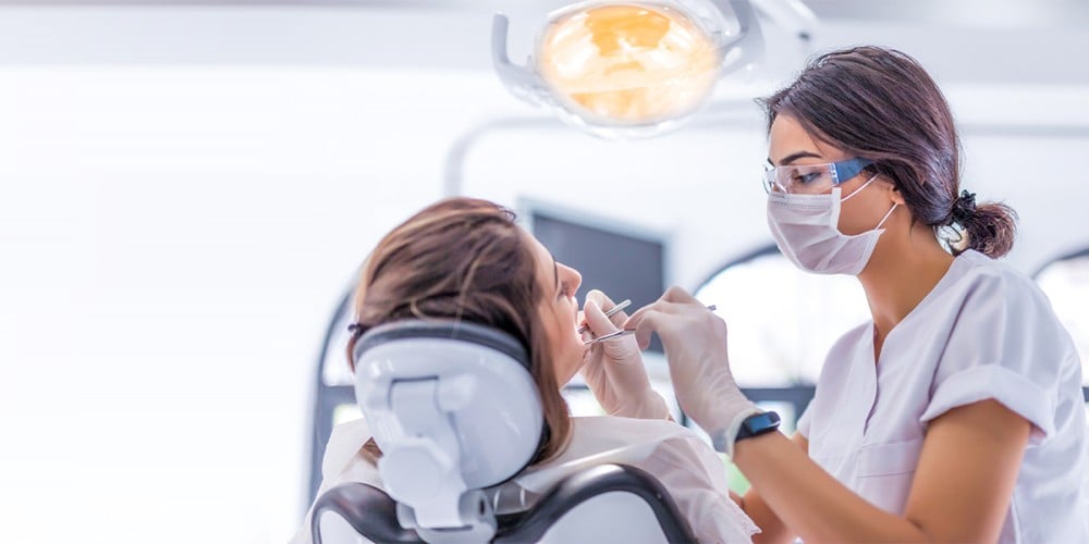 Une dentiste souriante porte un masque, un uniforme médical et des gants
