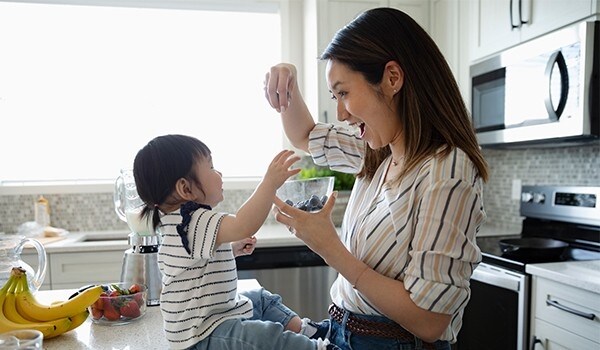 A young woman being playful with her kid while preparing a fruit smoothie